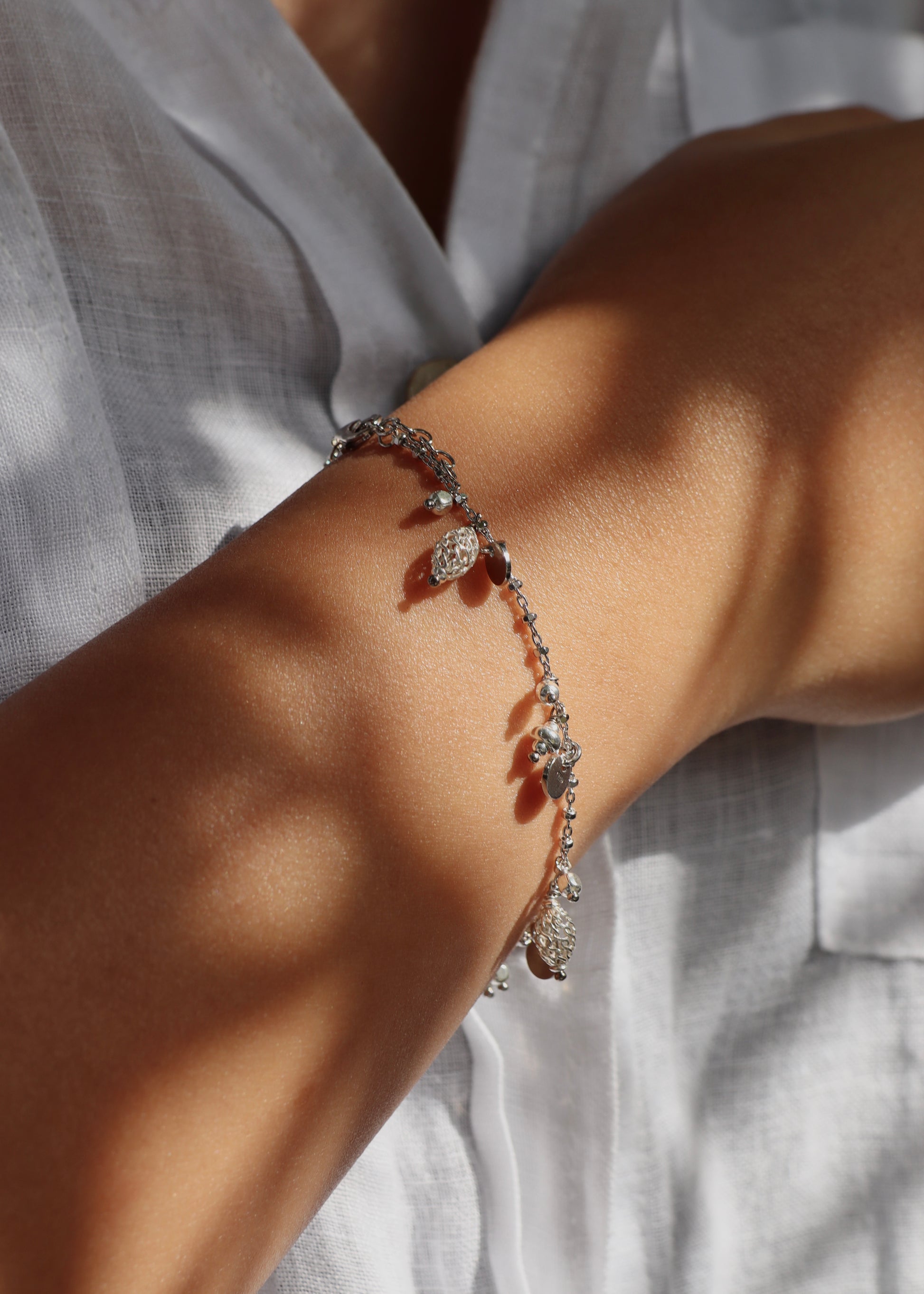 Bracciale Little Princess Monochrome Laura Sciunnach in argento 925 indossato al polso, con ciondoli traforati, medagliette e pepite. Gioiello artigianale Made in Italy dal design elegante e raffinato.
