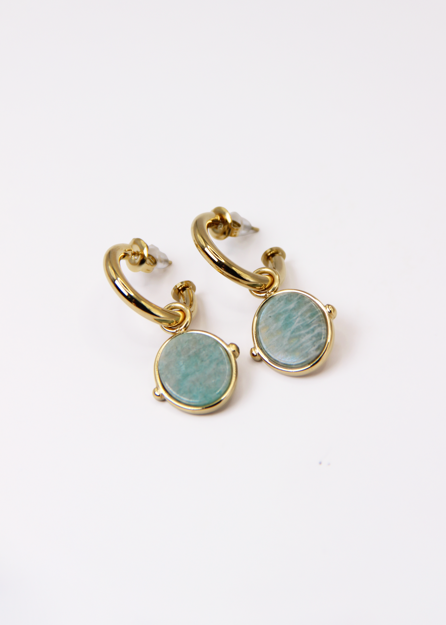 Orecchini a cerchio in acciaio placcato oro con pendente ovale in pietra dura naturale. Modello elegante con chiusura a perno, disponibile in vari colori tra cui occhio di tigre, malachite e opalite. Ogni pietra presenta leggere variazioni naturali di colore e venature.