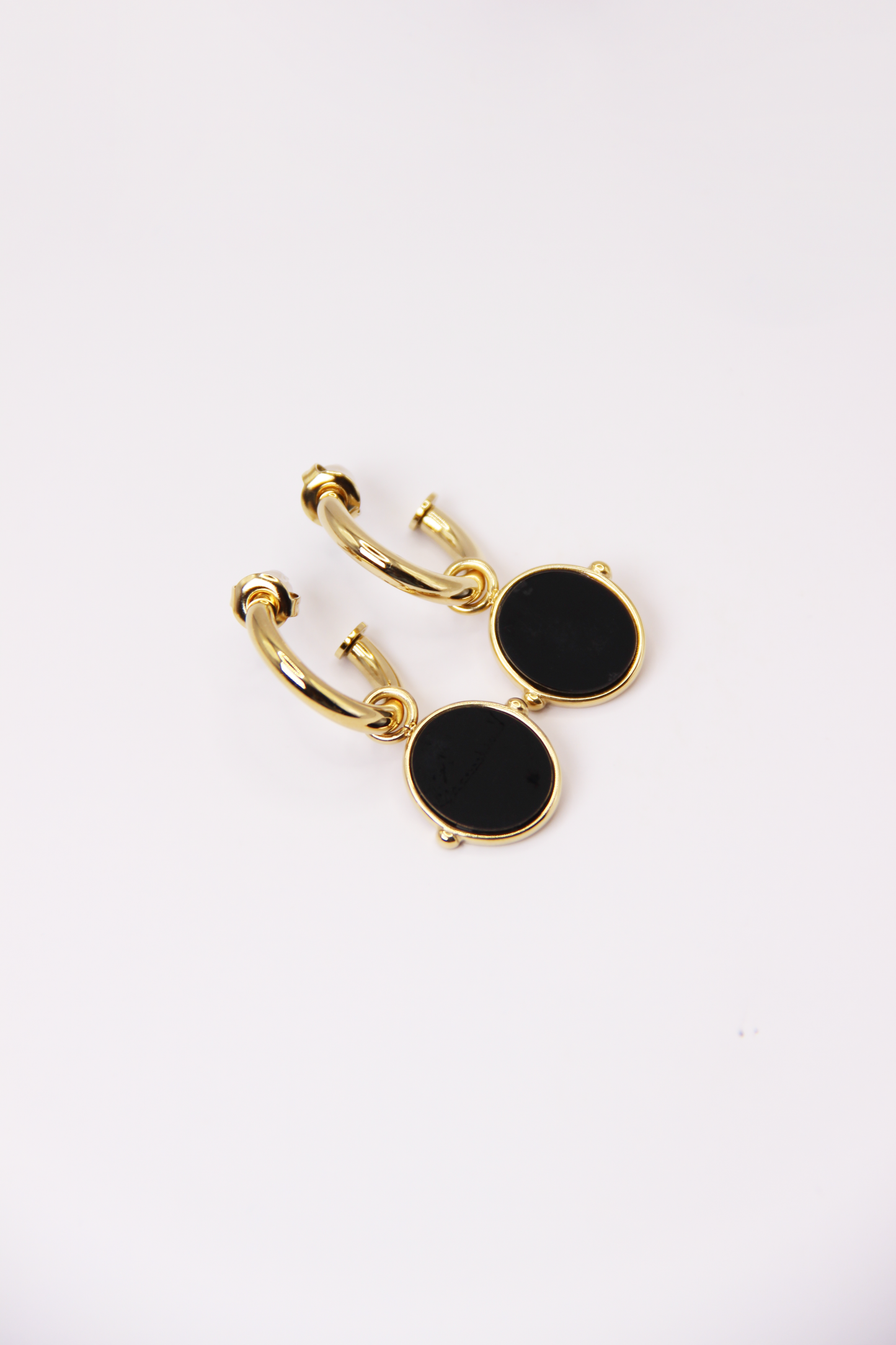 Orecchini a cerchio in acciaio placcato oro con pendente ovale in pietra dura naturale. Modello elegante con chiusura a perno, disponibile in vari colori tra cui occhio di tigre, malachite e opalite. Ogni pietra presenta leggere variazioni naturali di colore e venature.