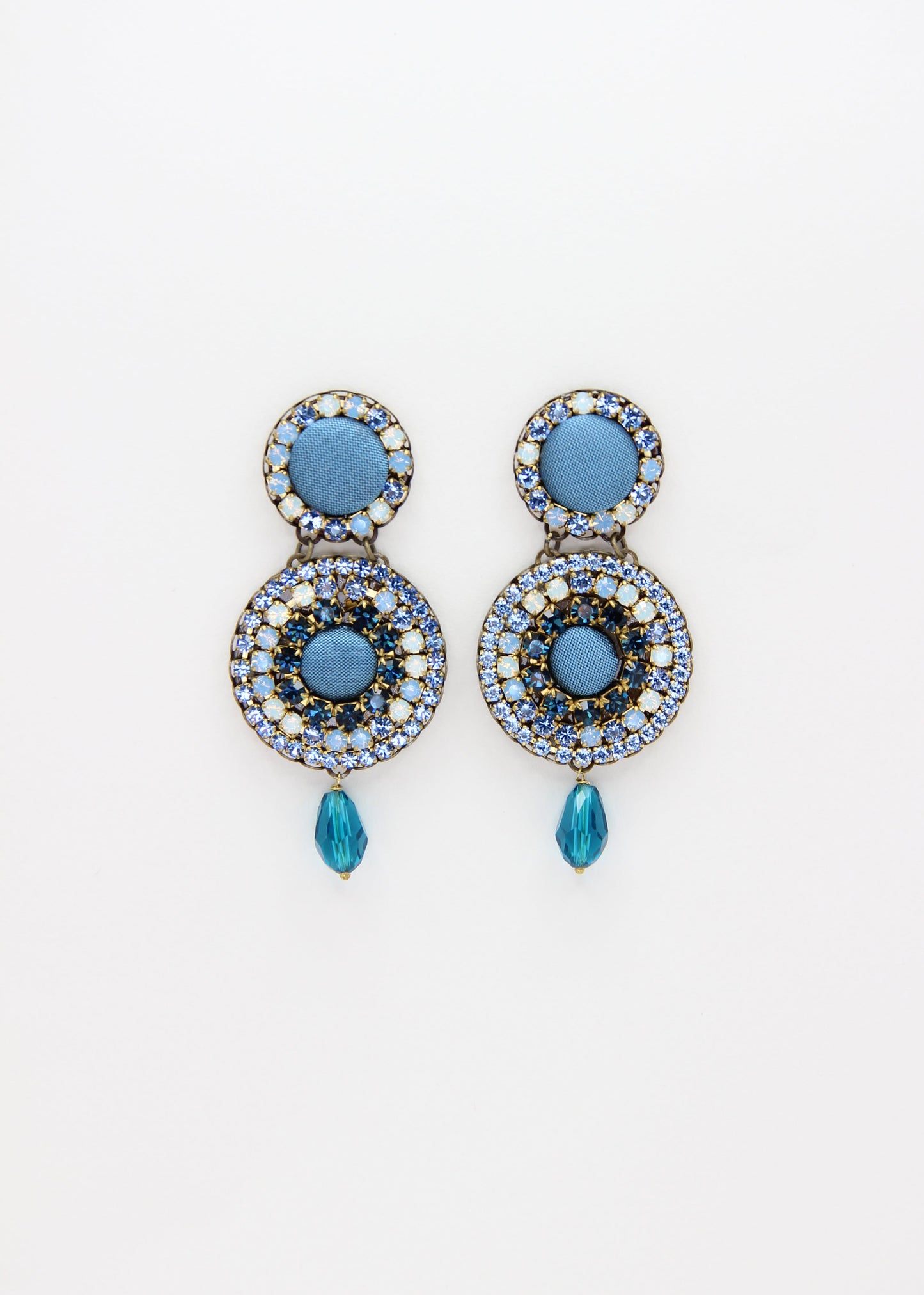 Orecchini artigianali Metropolitan Dubai azzurro, con bottoni circolari in tessuto color carta da zucchero, cristalli in gradiente azzurro e blu e pendente a goccia in cristallo. Nickel free, ideali per cerimonie ed eventi speciali.
