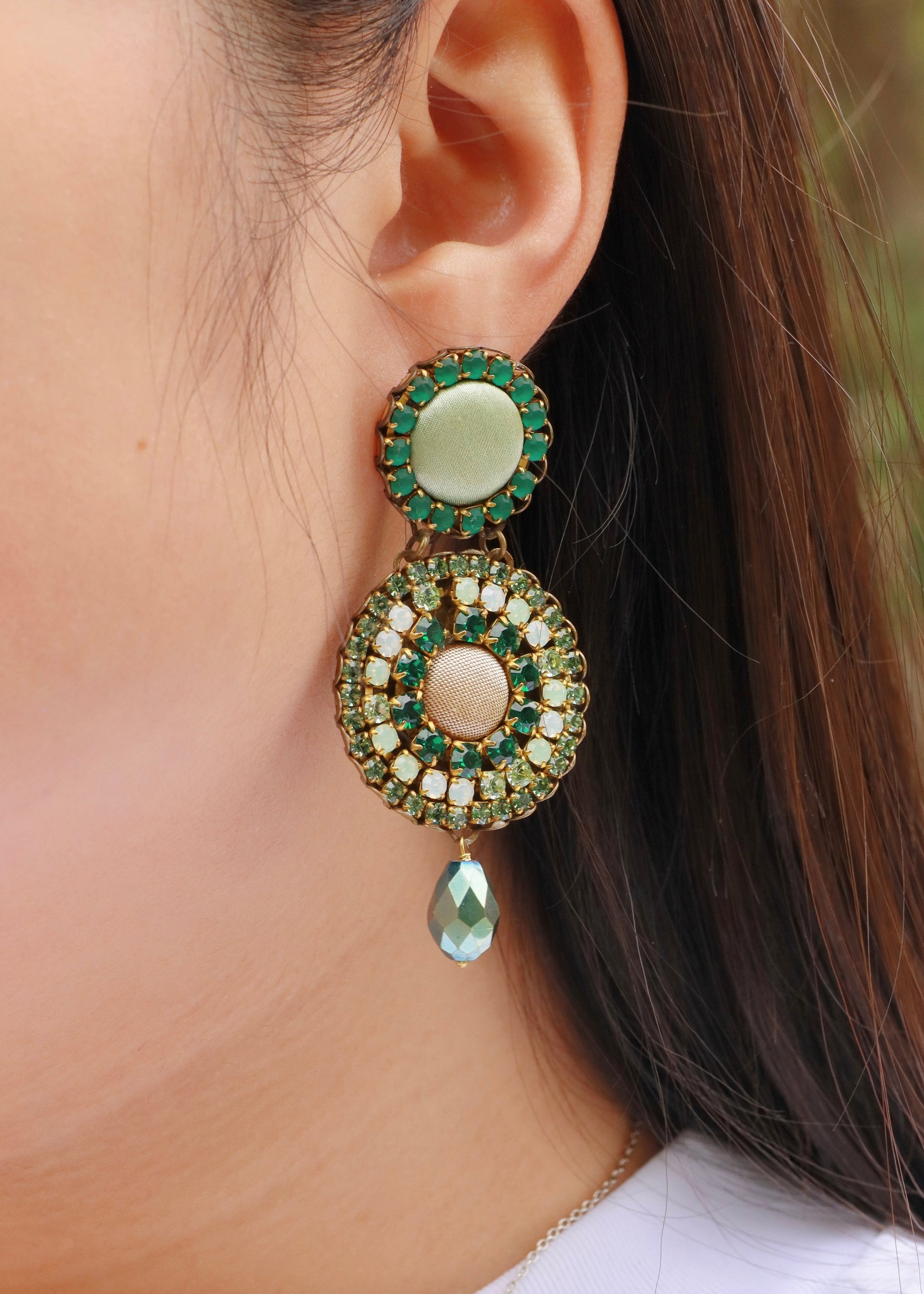 Orecchini artigianali Metropolitan Dubai verde, con bottoni circolari in tessuto color verde salvia, cristalli in gradiente verde e pendente a goccia in cristallo. Nickel free, ideali per cerimonie ed eventi speciali.
